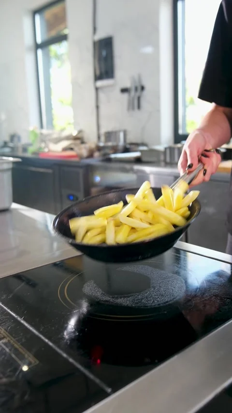 Skilled cook in a professional kitchen expertly tossing sliced raw potatoes in a Stock Footage 318316553