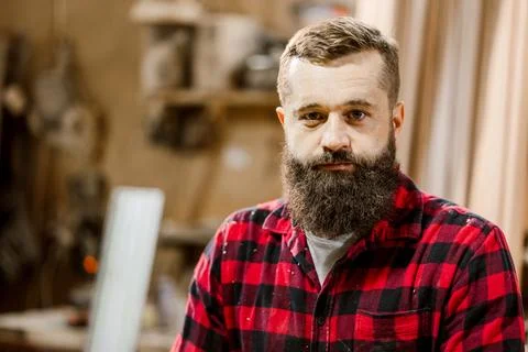 Skilled craftsman with beard standing in workshop surrounded by tools and wood Stock Photos