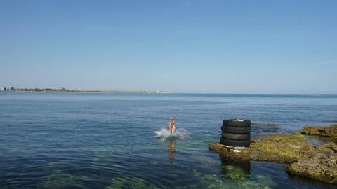 Skilled diver jumping to the deep blue sea from old tires on the coast. Stock Photos