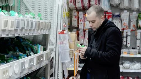 Skilled electrician checking light switch amid electrical supplies, evaluating Fotos Stock
