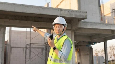 Skilled engineer inspects factory construction and uses a radio to chat with Stock Photos