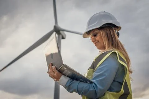 A skilled female engineer analyzes data at a wind turbine site, demonstrating Stock Photos