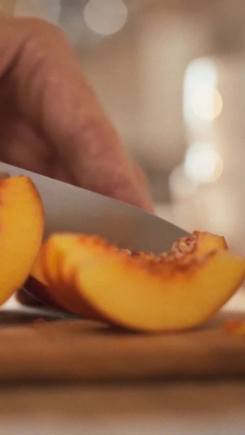 A skilled hand delicately slices a fresh juicy peach on a rustic wooden cutt Stock Footage 331531396