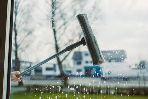 A skilled hand uses a squeegee to clean a window, removing droplets and strea Stock Photos