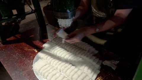 Skilled hands kneading and shaping noodles through a machine Stockbeeldmateriaal 327571283