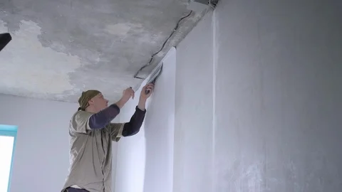 Skilled handyman cuts excess wallpaper pieces near ceiling Stock Footage 108582553