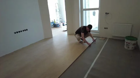 A skilled man diligently lays down new flooring in a vacant room as part of a re Video stock 343429795