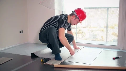 Skilled man with red helmet lay sub-flooring mat in new apartment Stock Footage 82068151