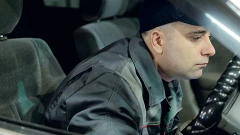 Skilled mechanic in baseball cap testing vehicle after servicing, gripping Fotos de archivo