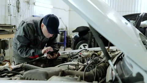 Skilled mechanic checking vehicle diagnostics on smartphone during engine Stock Footage 338217866