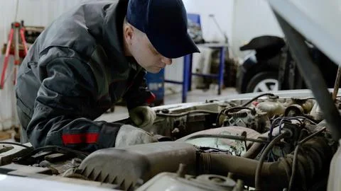 Skilled mechanic examining car engine, wearing protective gloves and performing Foto stock