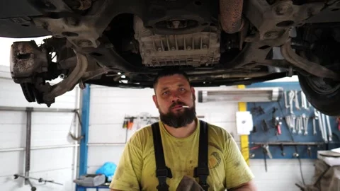 Skilled mechanic with a focused expression, working under a vehicle Stock-Footage 318725541