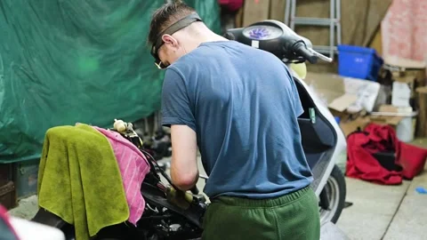 Skilled Mechanic Repairing Scooter Engine in a Cluttered Garage Workshop Stock Footage 344937701