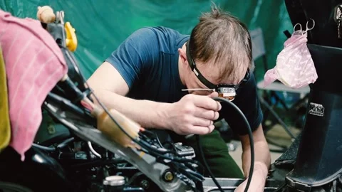 Skilled Mechanic Repairing Scooter Engine in Workshop with Headlamp Stock Footage 345726536