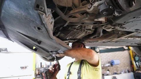 Skilled mechanic working under a vehicle, using a power tool Stock Footage 324501458