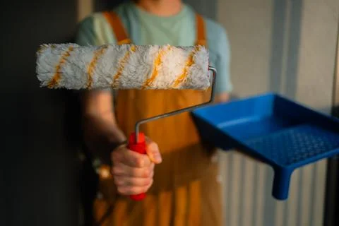 Skilled painter holding a paint roller with a red handle and a blue tray, ready Photos