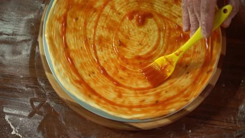 Skilled pizza maker puts ketchup on thick dough piece smearing sauce. Stock Footage 159370064