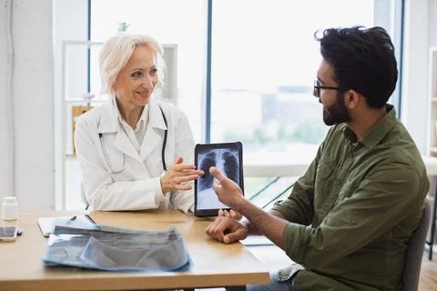 Skilled radiologist in white uniform explaining visible changes on x-ray image. 스톡 사진