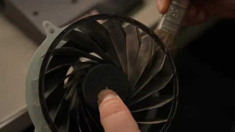 Skilled technician carefully brushing dust from gaming console cooling fan Stock Footage 307448129