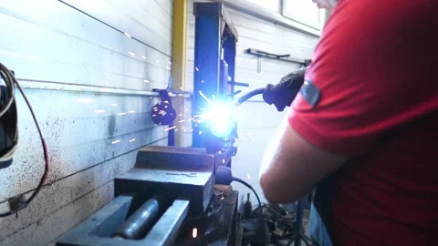 Skilled technician in protective gear welding metal piece in garage Stock-Footage 328643715