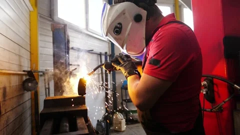Skilled technician in protective gear welding metal piece in garage Stock Footage 328643914
