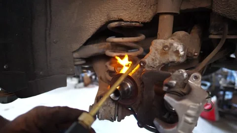 Skilled technician using a torch to heat a car component in a garage, showcasing Видео 334663803