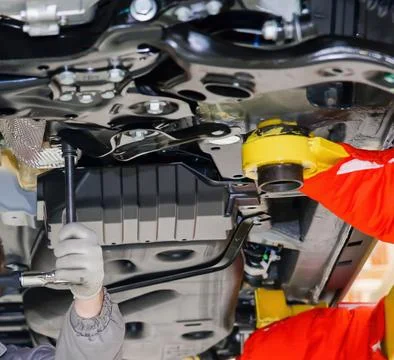 Skilled technicians work on the underside of a car, using tools to conduct re Stock Photos