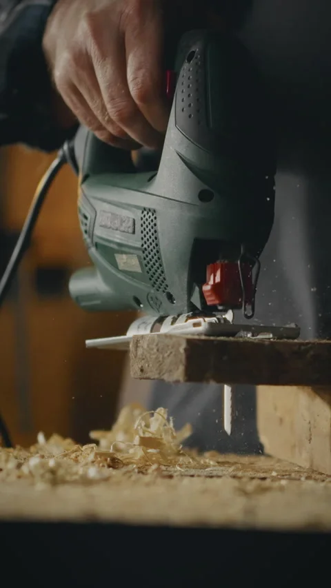 Skilled woodworker operates electric jigsaw to cut wood in workshop filled w Stock Footage 331727570
