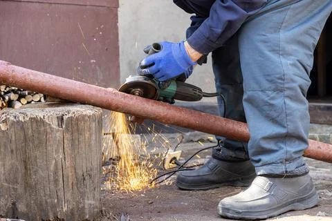 A skilled worker cuts a rusted metal pipe with an electric angle grinder ou.. Stock Photos