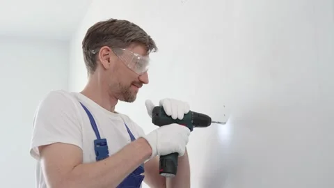 Skilled worker drilling hole in white wall, wearing protective gear during home Stock Footage 308487849