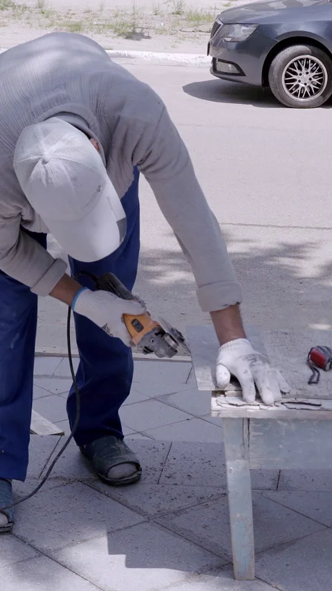 Skilled worker in gray attire uses power tools on a wooden surface outdoors Stock Footage 313926236