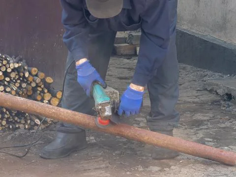 A skilled worker grinds a rusty metal pipe with a handheld angle grinder at.. Stock Photos