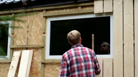 Skilled worker installing wooden panels on exterior wall, camera pans upward Stock Footage 322117679