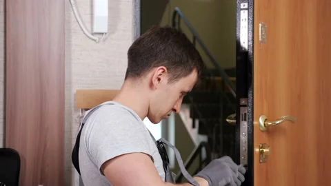 Skilled worker in uniform fixes front door lock in flat room Video stock 153150211