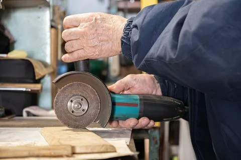 A skilled worker uses an angle grinder to shape a piece of wood on a workbench, Stock Photos