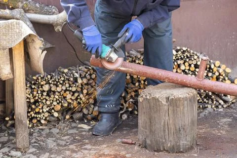 A skilled worker uses an electric angle grinder to cut a metal pipe outdoor.. Stock Photos