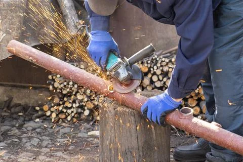 A skilled worker uses an electric angle grinder to cut a metal pipe on a wo.. Stock Photos