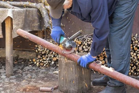 A skilled worker uses an electric angle grinder on a metal pipe with flying.. Stock Photos