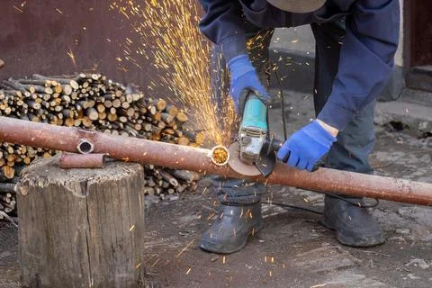 A skilled worker uses an electric angle grinder to cut a rusted metal pipe .. Stock Photos