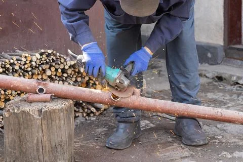 A skilled worker uses an electric angle grinder on a rusty metal pipe in an.. Stock Photos