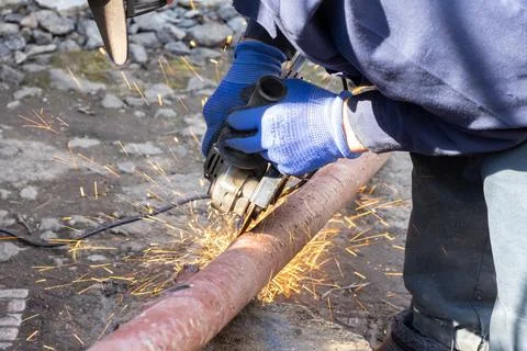 A skilled worker uses an electric angle grinder to cut a metal pipe outdoor.. Stock Photos