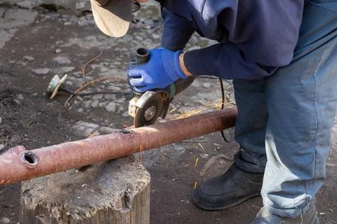 A skilled worker uses an electric angle grinder to cut a metal pipe outdoor.. Stock Photos