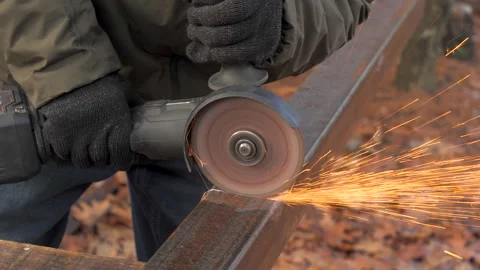 Skilled worker uses grinder to cut metal, creating sparks in outdoor workshop Stock Footage 297539736