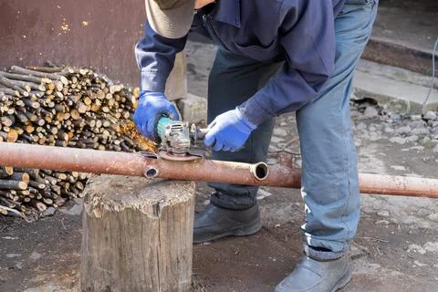 A skilled worker uses a power angle grinder to cut a metal pipe on a wooden.. Stock Photos