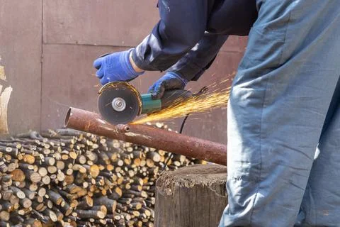 A skilled worker uses a power grinder to cut a rusty metal pipe, creating b.. Stock Photos