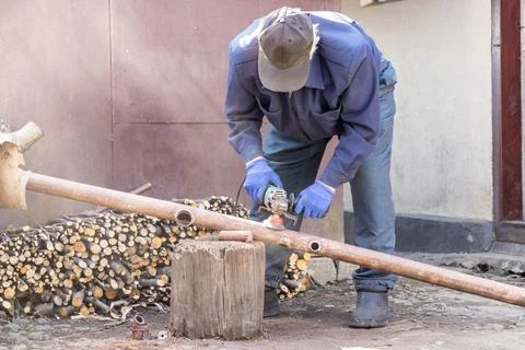 A skilled worker uses a power grinder to smooth a rusty metal pipe on a woo.. Stock Photos