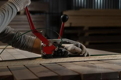 A skilled worker uses a strapping tool on wooden boards in a workshop. Stock Photos