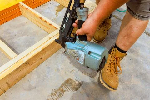 Skilled worker using nail gun for construction on wooden beams in workshop Stock Photos