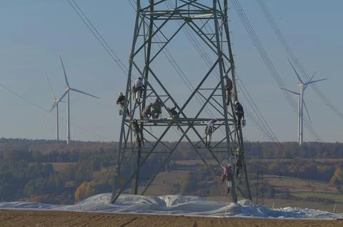 Skilled workers paint a towering high-voltage mast. Stock Photos