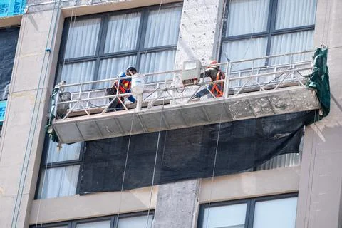 Skilled workers on suspended scaffold performing repairs on tall building Stock Photos